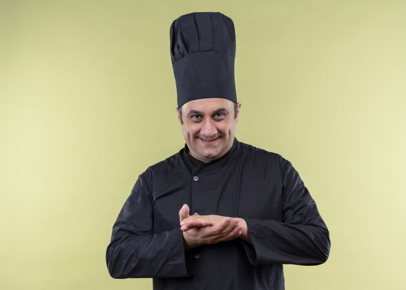 男性男厨师身穿黑色制服 头戴厨师帽 手牵着手 狡猾地微笑着看着镜头 站在绿色的背景上戴着狡猾绿色