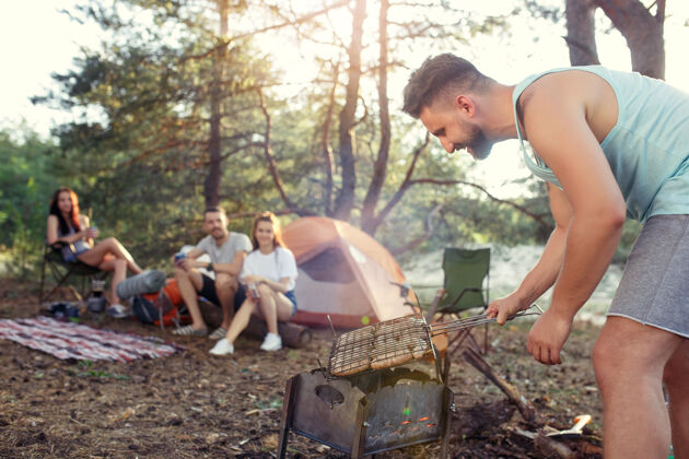 团体聚会 男女露营在森林里他们放松 唱歌 在绿草上烧烤度假 夏天 冒险 生活方式 野餐的概念冒险风景情侣