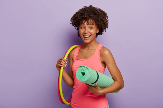 锻炼快乐的短发运动型女人拿着卷起的垫子 两个呼啦圈 穿着粉色背心 在健身房锻炼乐观训练运动