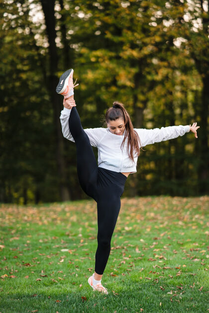 强壮穿着运动服的女人站在公园里做劈腿伸展健康姿势