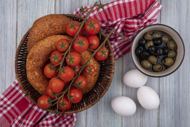 藤蔓新鲜的葡萄藤西红柿放在桶上 百吉饼放在布袋上 橄榄放在碗上 鸡蛋放在灰色的木制背景上衣服鸡蛋碗