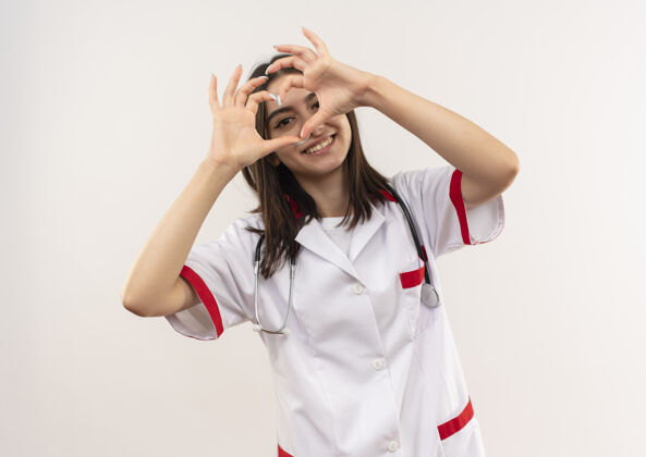 心脏年轻的女医生身穿白大褂 脖子上戴着听诊器 站在白墙上露出友好微笑的心形女人医生人
