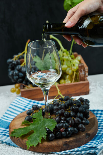 盘子把葡萄酒倒进杯子里 把一盘葡萄放在白色的桌子上手暗的杯子