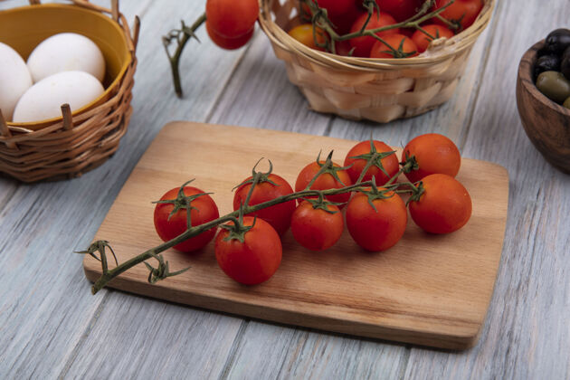 蔬菜新鲜的红色西红柿放在木制厨房板上 藤蔓西红柿放在桶上 有机鸡蛋和橄榄放在灰色木制背景上餐食物藤蔓