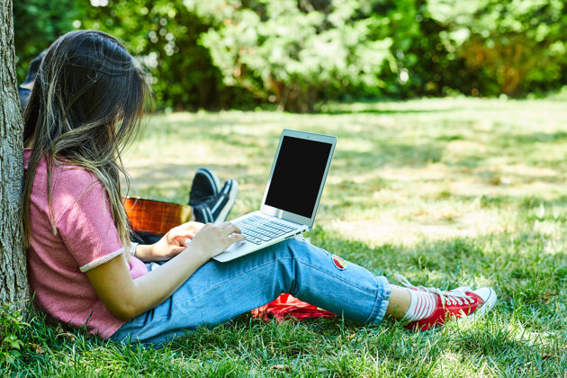 现代坐在绿草上使用笔记本电脑的年轻女子公园独处夏天