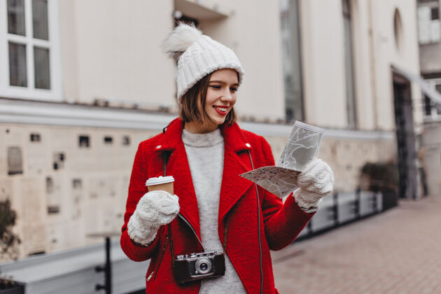漂亮戴着白帽子 穿着红大褂的美丽游客拿着地图 探索着城市建筑物背景上戴着手套的女孩的画像时尚女士成人