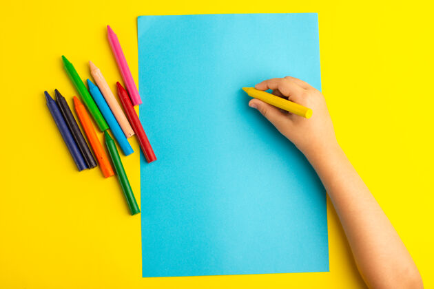 钢笔俯视图：小孩用彩色铅笔在黄色的蓝色纸上画铅笔绘画绘画