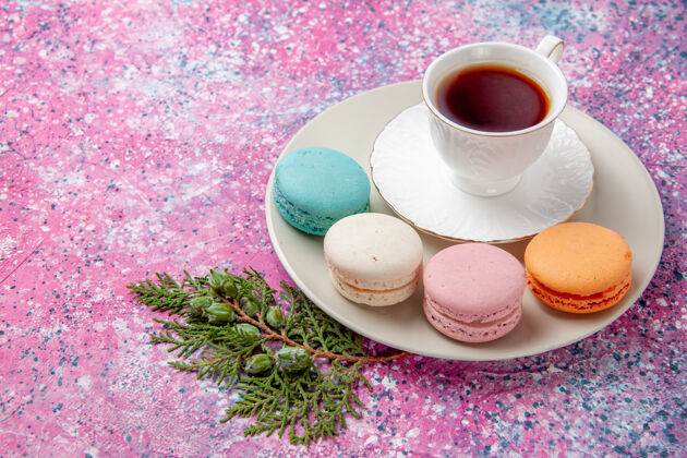 派顶视图一杯茶 粉色表面有五颜六色的法国马卡龙饼干茶碟饮料