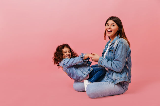 关系快乐的白人妇女和女儿玩耍摄影棚拍摄的粉红色背景下 一个卷发的孩子和妈妈坐在一起妈妈父母成人