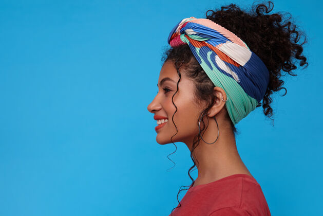 爱情年轻迷人的黑发女人的侧视图 卷曲的头发 站在蓝色的墙上 带着真诚的微笑 愉快地看着前方发型休闲积极