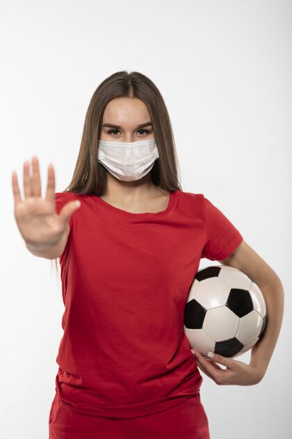 运动戴着面具拿着球并显示停止标志的女足球运动员女足球足球制服