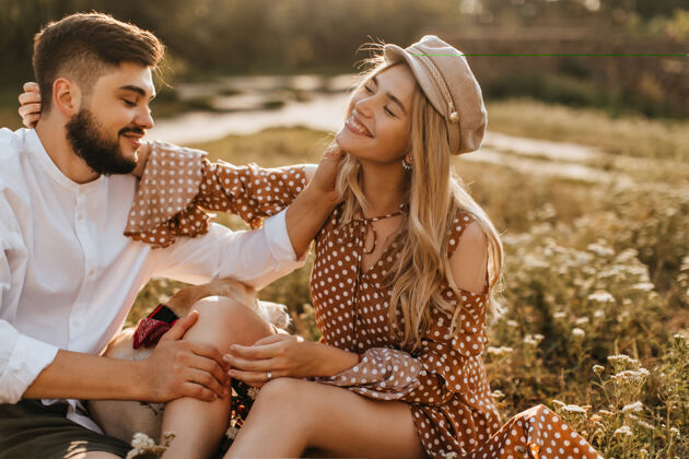 年轻男人和女人坐在草地上轻轻地抚摸对方浪漫的情侣微笑着和拉布拉多合影圆点连衣裙狗欢呼