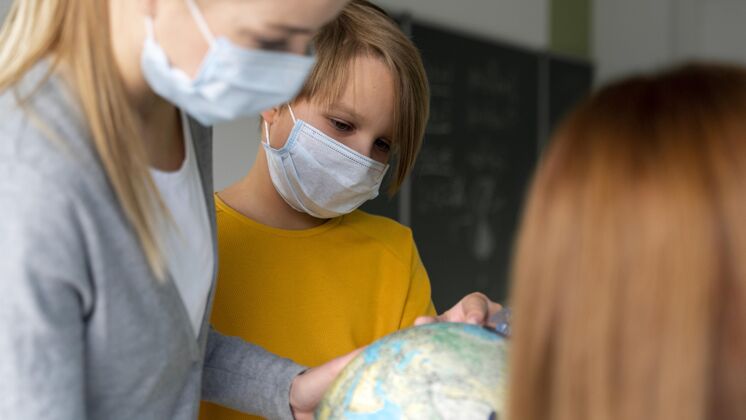 新常态带着医用面罩的女教师在教室里用地球仪教地理返校流行病学校