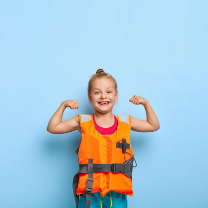 生活可爱的小孩举起双臂 露出肌肉 穿着橙色充气救生衣学前班充气孩子