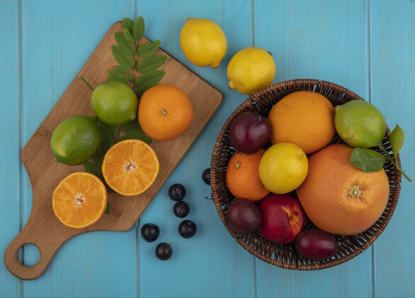 水果俯视图：在一篮柚子 橙子 柠檬 酸橙和樱桃李子中混合水果 在绿松石色背景上放一个砧板葡萄柚视图绿松石