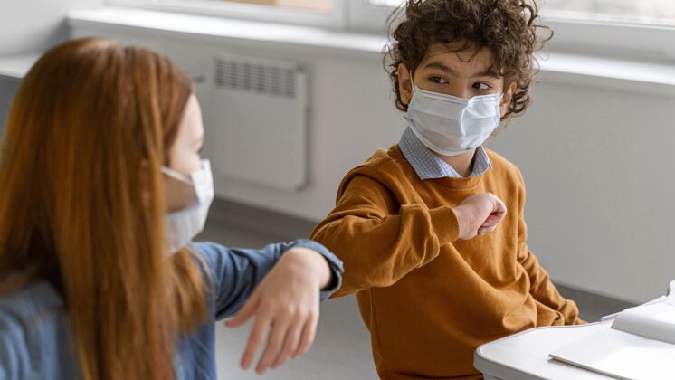 冠状病毒戴着医用口罩的孩子在课堂上做肘部敬礼病毒学生新常态