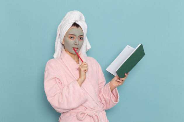 女正面图年轻女性穿着粉色浴袍淋浴后拿着复写本在蓝色墙壁上美容水霜自理淋浴浴室奶油肖像抄写本