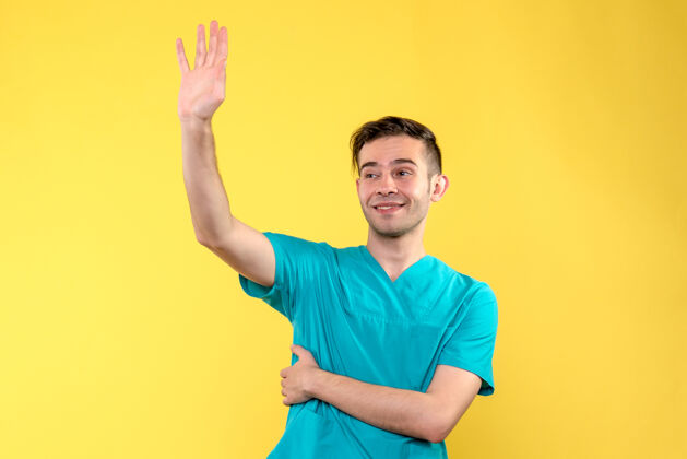 医学黄色墙上挥手的男医生的正面图健康看挥手