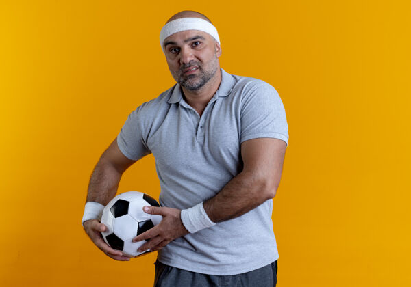 姿势成熟的运动型男人戴着头巾 手里拿着足球 面带严肃的表情站在橘色的墙上向前看运动市民足球