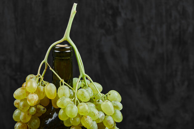 自然白葡萄和一瓶葡萄酒在黑暗的表面季节新鲜食物
