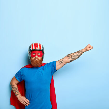 斗篷严肃自信的超级英雄假装飞翔 戴着红色斗篷 面具 防护头盔成功胡子力量
