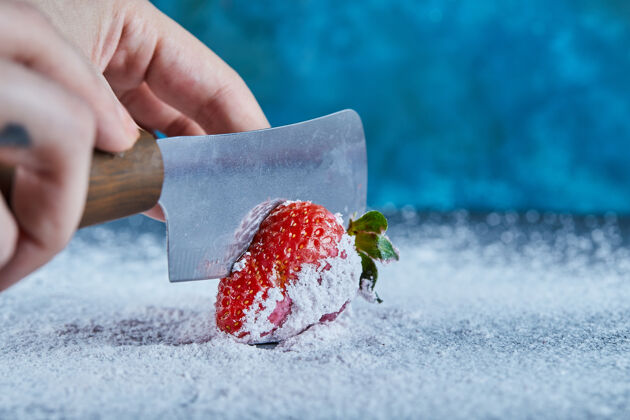 切用刀在蓝色表面切新鲜草莓的女人可食用草莓闪亮