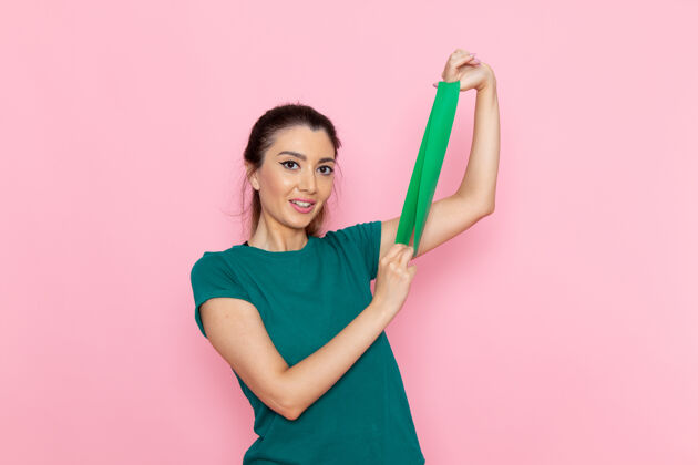 抱着正面图年轻女性拿着绿色绷带在粉红色的墙上美容运动运动员锻炼苗条人微笑欢呼