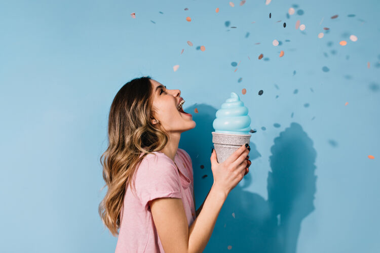 女性可爱的黑发女人拿着冰淇淋在蓝色的墙上摆姿势室内冰淇淋乐趣