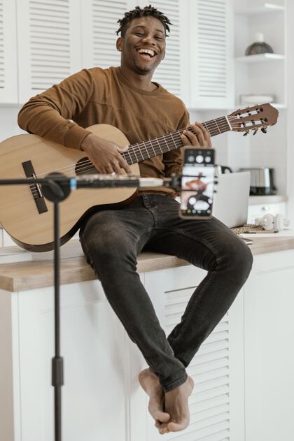 垂直笑脸男音乐家在家里弹吉他和手机录音的正面图音乐家乐器手熟练程度