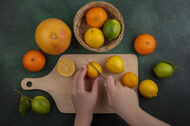 葡萄柚俯瞰图：一位女士在砧板上切柠檬 绿色背景上放着酸橙和葡萄柚食品酸橙柠檬