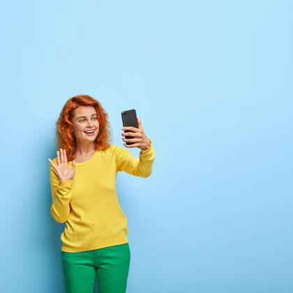 风格可爱的红发女人打视频电话 和亲戚聊天 对着镜头挥手 友好的微笑红发在线掌上电脑