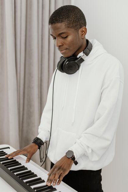 艺术家男音乐家在家玩电子键盘的侧视图耳机乐器手房子