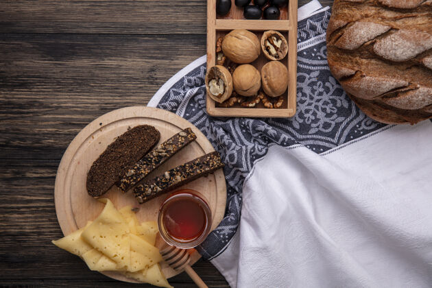 黑色顶视图蜂蜜在一个罐子里 黑面包和奶酪放在一个架子上 核桃放在木制的背景上核桃甜味面包