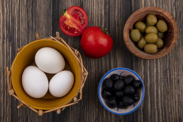 鸡肉顶视图：篮子里的鸡蛋 碗里的黑橄榄和绿橄榄 木制背景上的西红柿营养番茄景观