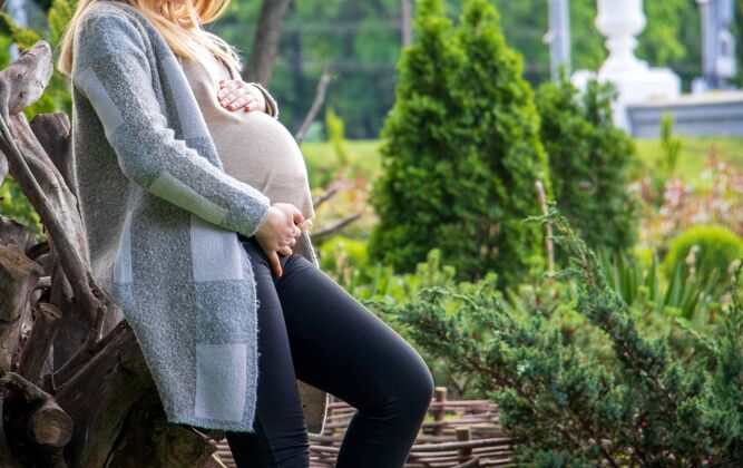 阳光特写镜头中的一位孕妇穿着开衫抱着她的肚子在花园-母亲的概念为人父母自然女性