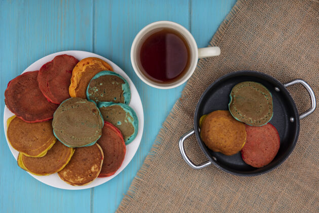 风景顶视图五颜六色的煎饼在盘子上和煎锅里 茶杯放在米色餐巾上 背景是绿松石色薄煎饼盘子薯条