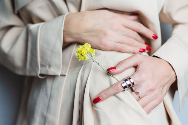 户外近距离拍摄的女人手上的红色指甲两环穿着米色西装黄色可爱的干花在口袋里护理新娘裸色