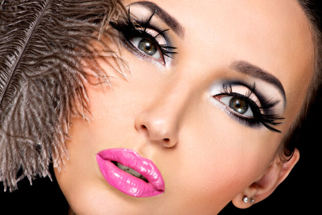 外观美丽的女人用明亮的专业化妆品和羽毛靠近脸女人制作羽毛