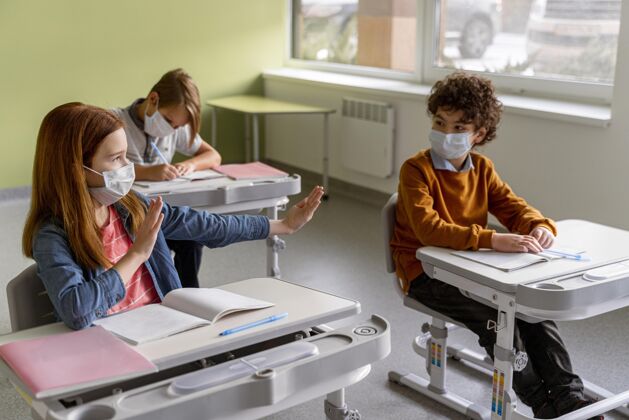流行病高角度的孩子戴着医用口罩在教室里保持距离学习知识病毒