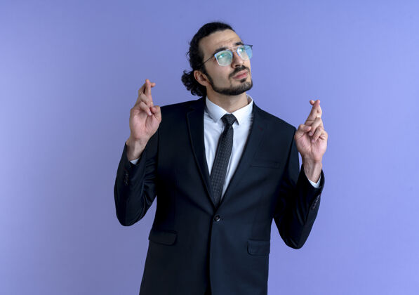 男人一个穿着黑西装戴着眼镜的商人站在蓝色的墙上一边许愿生意人看人