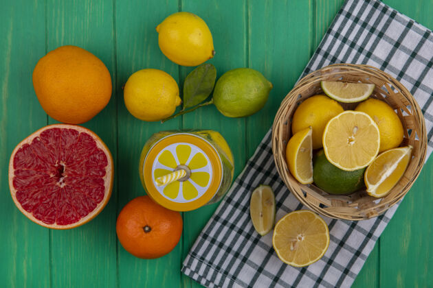 橘子顶视图柠檬柠檬片放在一条格子毛巾上 橘子和半个柚子放在绿色的背景上上衣绿色玻璃
