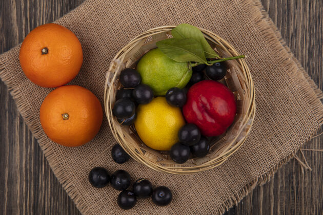 食物顶视图樱桃李子 柠檬酸橙和桃子放在篮子里 橘子放在米色餐巾上柠檬橘子桃子