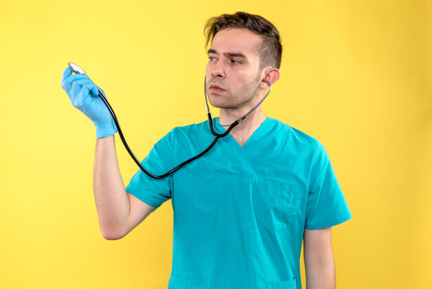 成人黄色墙上手持听诊器的男医生的正视图男性医生健康听诊器