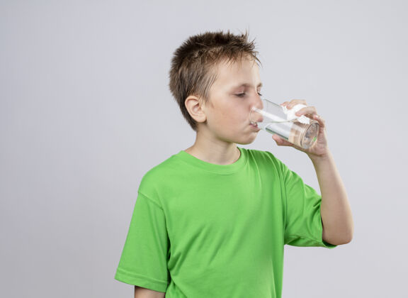 感觉生病的小男孩穿着绿色t恤 站在白墙上喝水 感觉不舒服疾病小男孩