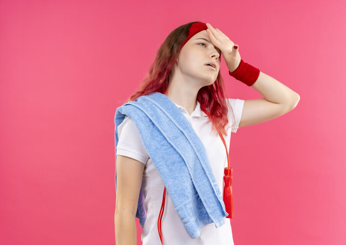 女戴着头巾 肩上扛着毛巾 站在粉红色的墙上 看上去疲惫而疲惫的年轻运动女性肩膀累运动装
