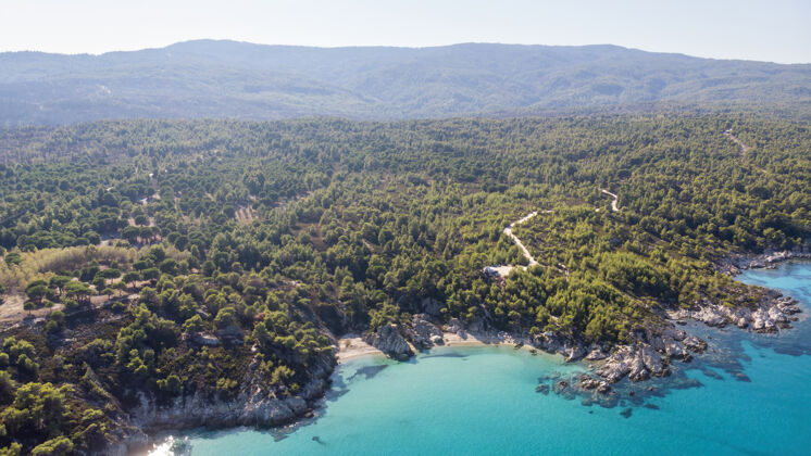 观点爱琴海沿岸有蓝色透明的海水 周围绿树成荫 岩石 灌木丛和树木 从无人驾驶飞机上俯瞰希腊岩石山海滩