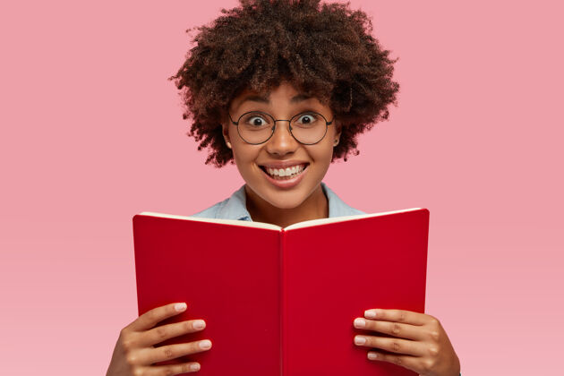 课本横拍的是一个面带微笑的漂亮女孩 带着课本 戴着眼镜 准备考试 隔着粉红色的墙人 种族和文化观念高兴携带高兴