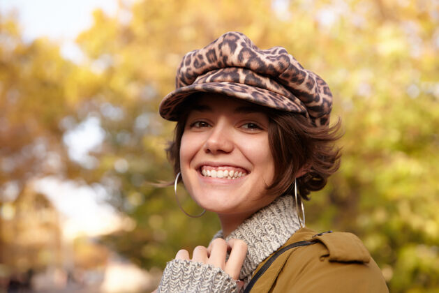 温暖可爱快乐的年轻黑发女子戴着豹纹帽子 站在迷离的公园里 面带迷人的笑容 快乐地看着理发微笑爱情