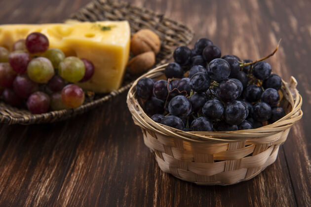 壁板侧视图黑色葡萄在一个篮子里与各种奶酪和坚果在一个木制背景上的立场葡萄新鲜收获