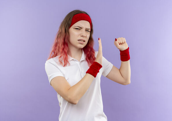 市民一个年轻的运动女人站在紫色的墙上做着一个握拳防守的姿势 带着厌恶的表情运动服姿势运动